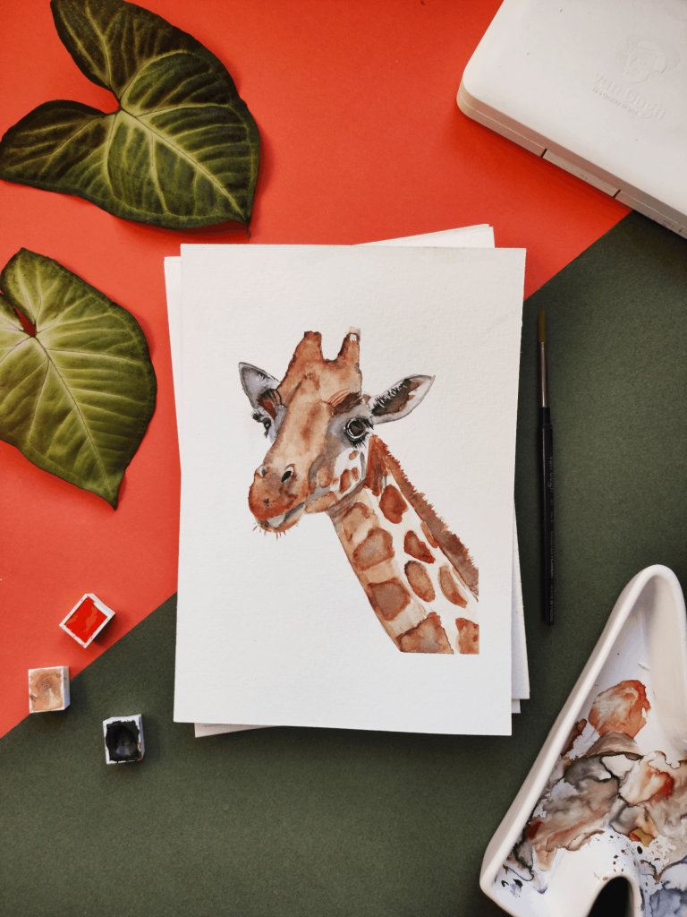 A watercolor painting of a giraffe surrounded by leaves and painting tools.